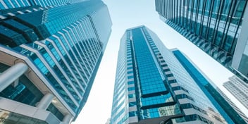 Upward view of modern skyscrapers with glass facades reflecting the sky, creating a sleek and futuristic look. Ideal for business or urban architecture.