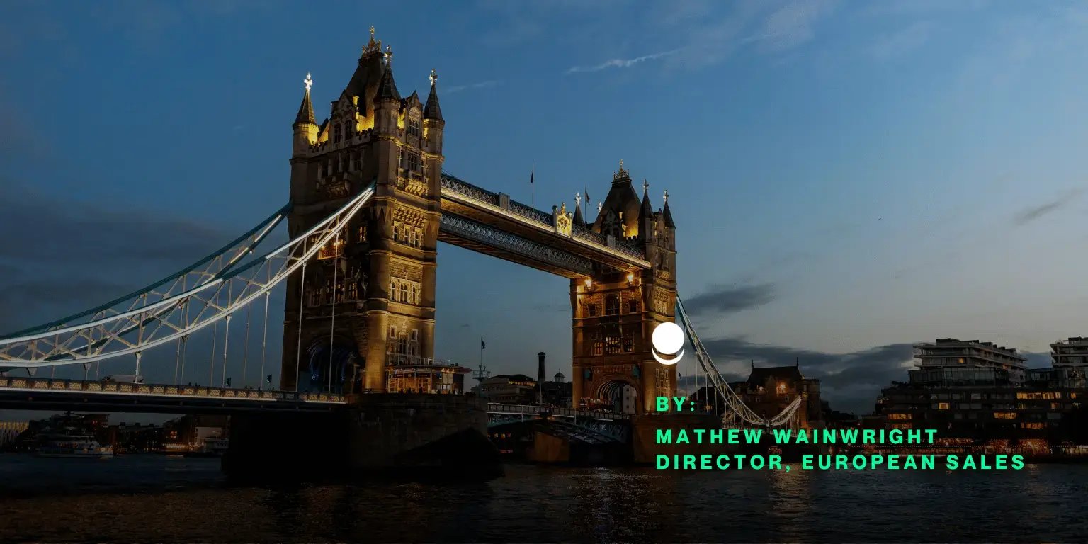  Night view of Tower Bridge in London, illuminated with warm lights, against a cloudy evening sky, with text overlay partially visible in green and white. 