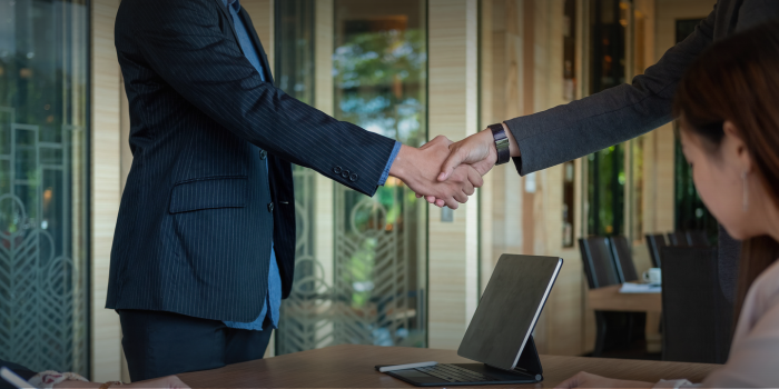  Two business professionals shaking hands across a table in a corporate setting. 