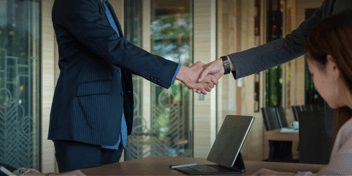 Two business professionals shaking hands across a table in a corporate setting.