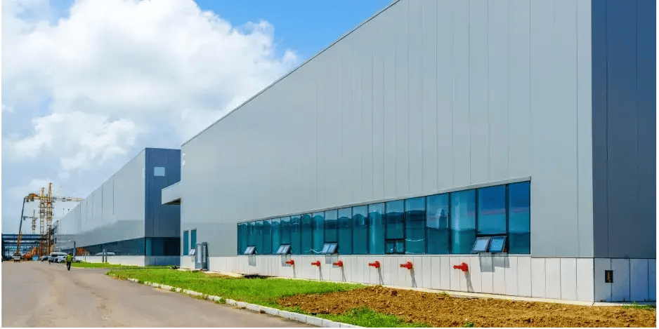  Modern industrial warehouse exterior with large windows, fire hydrant connections, and a clear blue sky. 