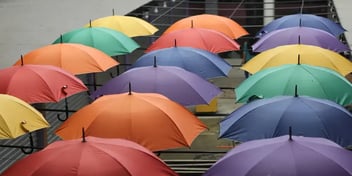 A row of colourful umbrellas in a line walking up a row of stairs