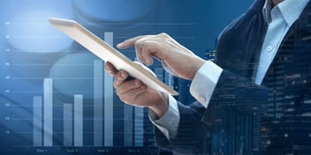 Close-up of a person's hands using a tablet with a background of bar charts and financial data, symbolizing business analytics and data-driven decision-making.