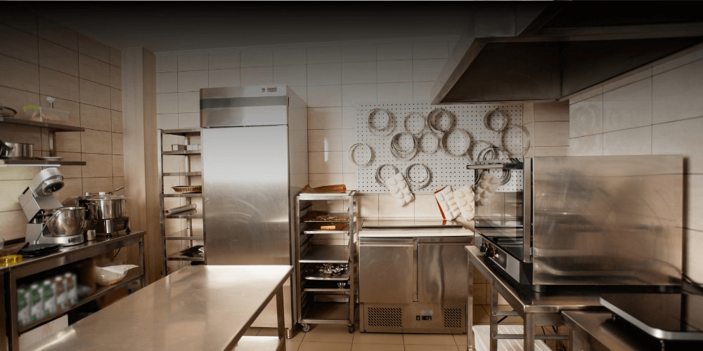  A commercial kitchen with stainless steel appliances, countertops, and storage racks. Pots and pans hang neatly on the wall, creating an organized and professional cooking space, illuminated by warm lighting. 