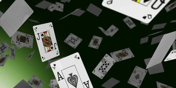 Playing cards scattered in mid-air against a dark background, featuring various suits and values, including an Ace of Spades and a King of Hearts. The arrangement gives a dynamic, floating effect, evoking a sense of movement and chance.