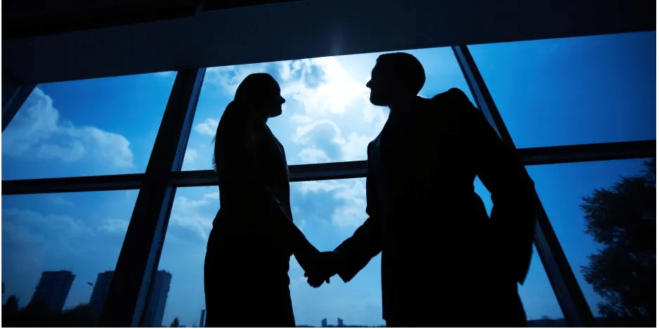  Silhouetted business professionals shaking hands in front of large windows with a cityscape background 