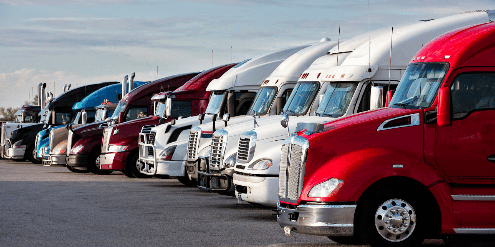  Row of red and white semi-trucks parked in a lot under a clear sky, showcasing a fleet of commercial vehicles lined up in an orderly manner. 