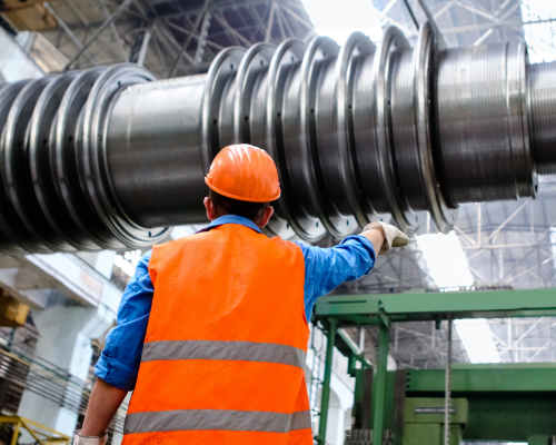 industrial manufacturing worker operating heavy machinery while wearing a safety vest and hard helmet